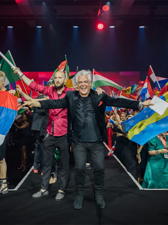 A man with arms outstretched, a crowd with national flags in the background