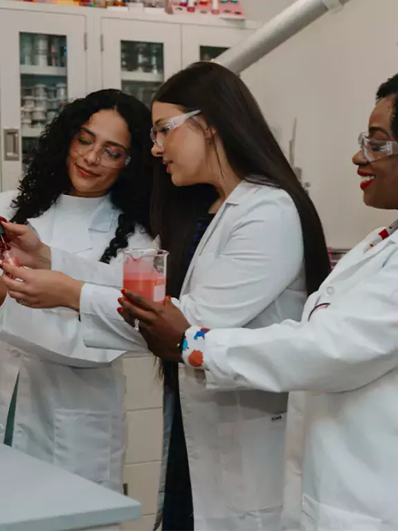 Three women in white coats holding a beaker in the laboratory